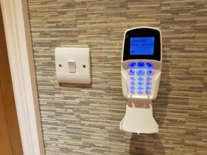 Modern white digital alarm keypad with LCD screen mounted on an interior wall for system arming