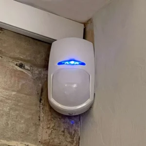 Discrete white Passive Infrared (PIR) sensor mounted in a room corner for volumetric motion detection